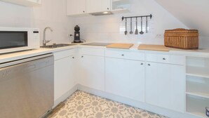 A compact kitchen with white cabinets, a microwave, a coffee maker, and a wicker basket on the countertop. - Beautiful apartment for 4 people with WIFI, TV and pets allowed (De Haan)
