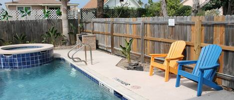 A swimming pool with a hot tub, surrounded by a wooden fence, and two Adirondack chairs.