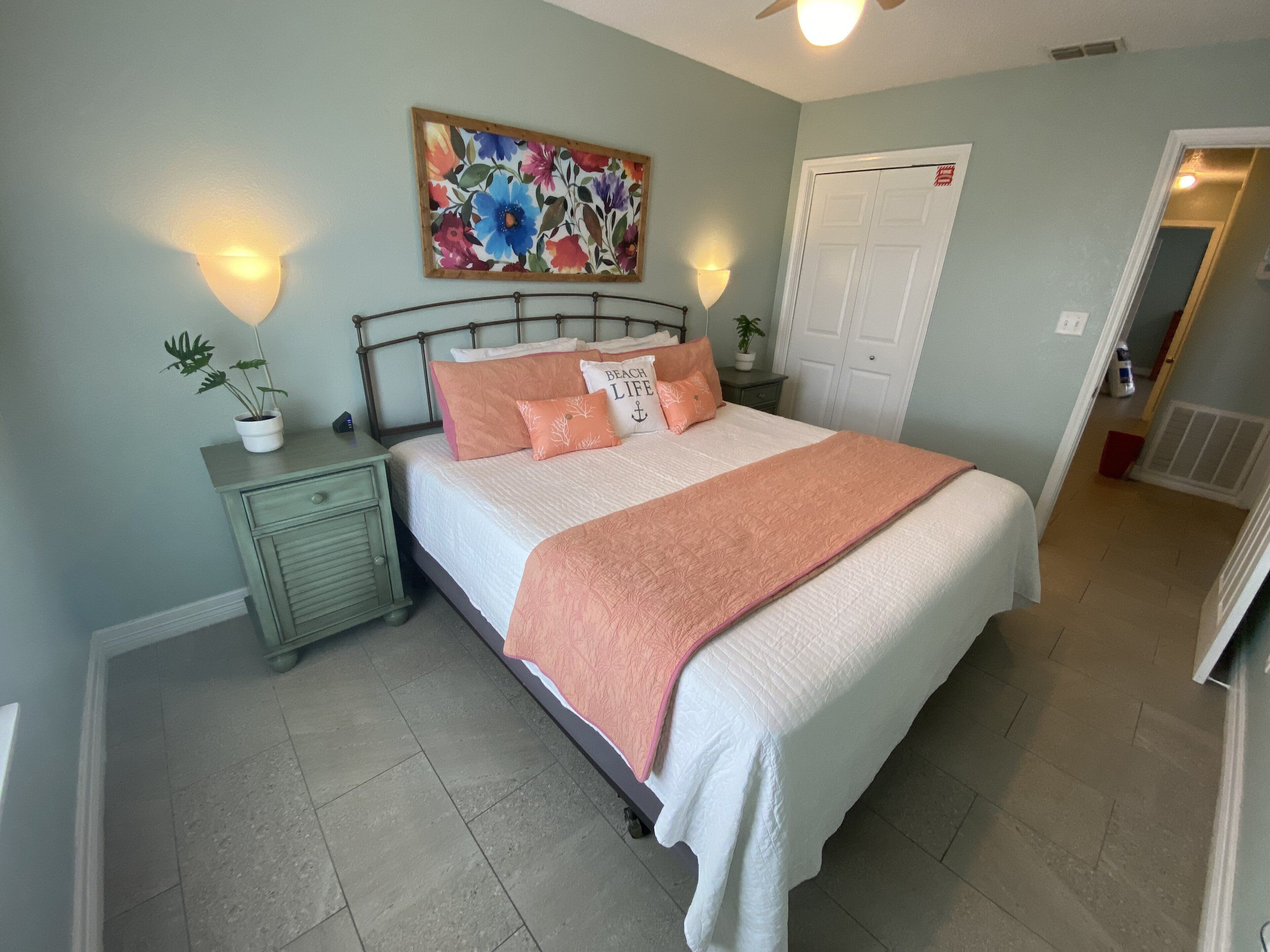 A bedroom with a bed, nightstands, a painting, and a door.