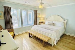 A bedroom with a bed, a bench, a desk, and a ceiling fan.