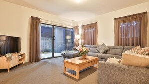 A modern living room with a flat-screen TV, a wooden coffee table, a grey sofa, and a sliding glass door leading to an outdoor area. - Modern 4 bedroom house with marina mooring, 2km from CBD (Mildura)