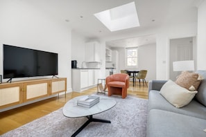 A modern living room with a flat-screen TV, a sofa, a coffee table, and a dining area with chairs.