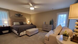 Une chambre à coucher comprenant un lit, des tables de chevet, une commode, une chaise et un ventilateur de plafond.