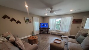 Un salon comprenant un canapé, un pouf, une table basse et un téléviseur posé sur un meuble.
