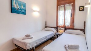 Una stanza con due letti singoli, un quadro con barche a vela, una finestra con tende in pizzo e un lampadario a parete.