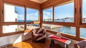 Una stanza con ampie finestre vista sulla costa, una poltrona marrone, un tavolino con una nave in miniatura e un pavimento piastrellato.