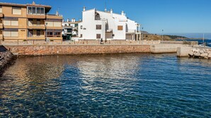 Un edificio costiero con un muro in pietra e acque blu cristalline davanti.