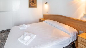 Un lit bien fait, avec du linge de lit et des serviettes blanches, une tête de lit en bois, une table de chevet avec une lampe et un tableau accroché au mur.