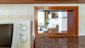 Une cuisine équipée d’un lave-linge et d’un sèche-linge intégrés, de plans de travail en granit et d’une fenêtre à cadre en bois donnant sur un espace de vie comprenant un canapé et une table.