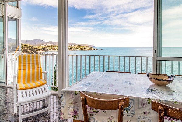A balcony with a view of the sea, a table with a floral tablecloth, and a striped chair.