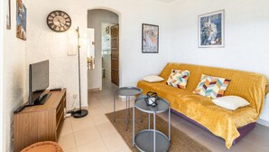 Una sala de estar acogedora con un sofá, un televisor, un reloj y una mesita.