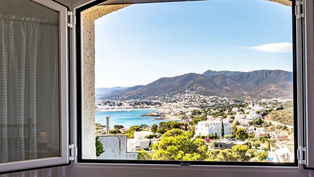 Vista desde una ventana sobre un pueblo costero con montañas al fondo.