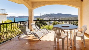 Un balcón con mesa y sillas, con vista a un paisaje costero con montañas y una masa de agua.