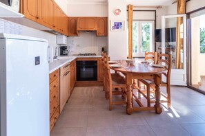 A compact kitchen with wooden cabinets, a built-in oven, and a dining table with chairs.
