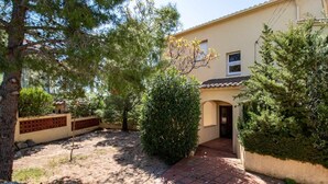 Una casa amb un carrer d'accés pavimentat, un petit jardí amb arbustos diversos i un teulat de teules.