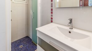 Een badkamer met een witte wastafel, een spiegel en een douchegedeelte met een blauwe betegelde vloer.