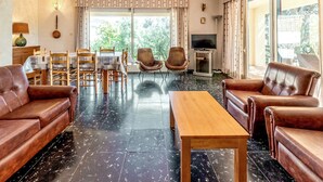 Un salon spacieux avec une table basse en bois, des canapés en cuir, une table à manger avec des chaises et un téléviseur.
