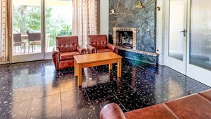 Un salon doté d’une cheminée en pierre, de canapés en cuir et d’une porte vitrée donnant sur un espace extérieur.