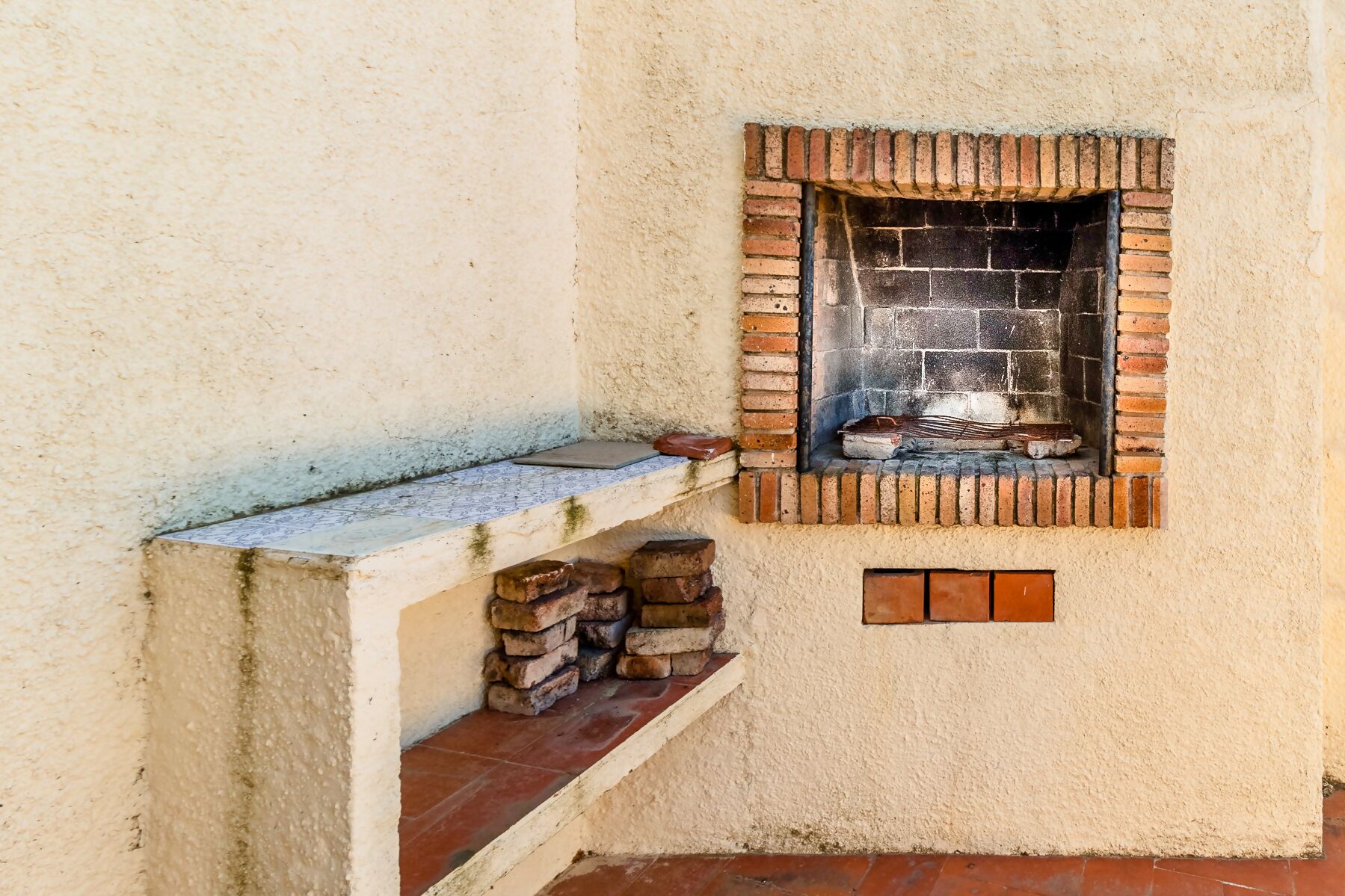 Ein kleiner, geschlossener Kamin aus Backsteinen mit Ablagefläche aus Stein darunter.