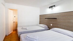 Hotellihuone, jossa on kaksi erillistä sänkyä, puinen pääty, pieni yöpöytä ja kylpyhuone, joka näkyy avoimesta ovesta.