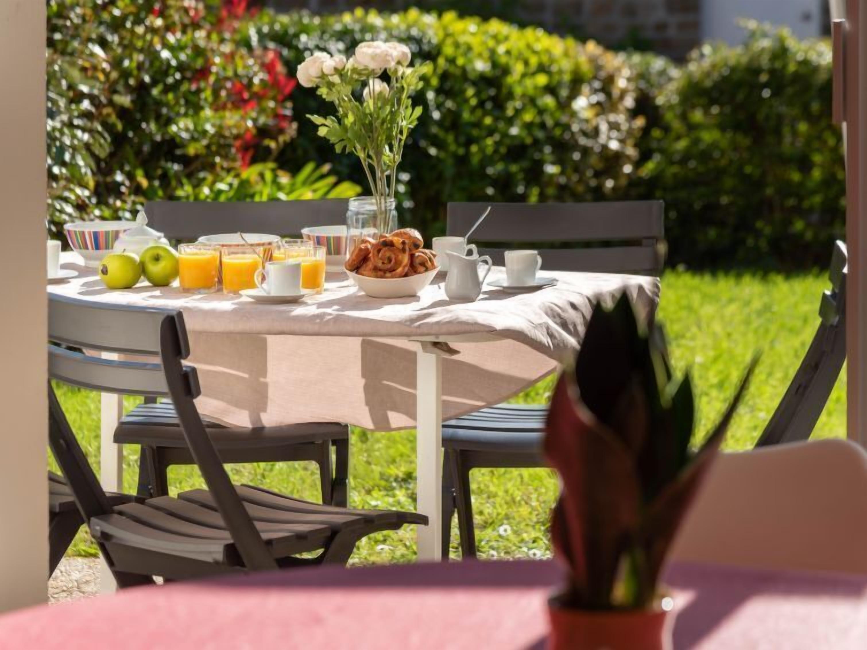 Un área de comedor al aire libre con una mesa preparada para el desayuno, incluyendo frutas, pasteles y bebidas.