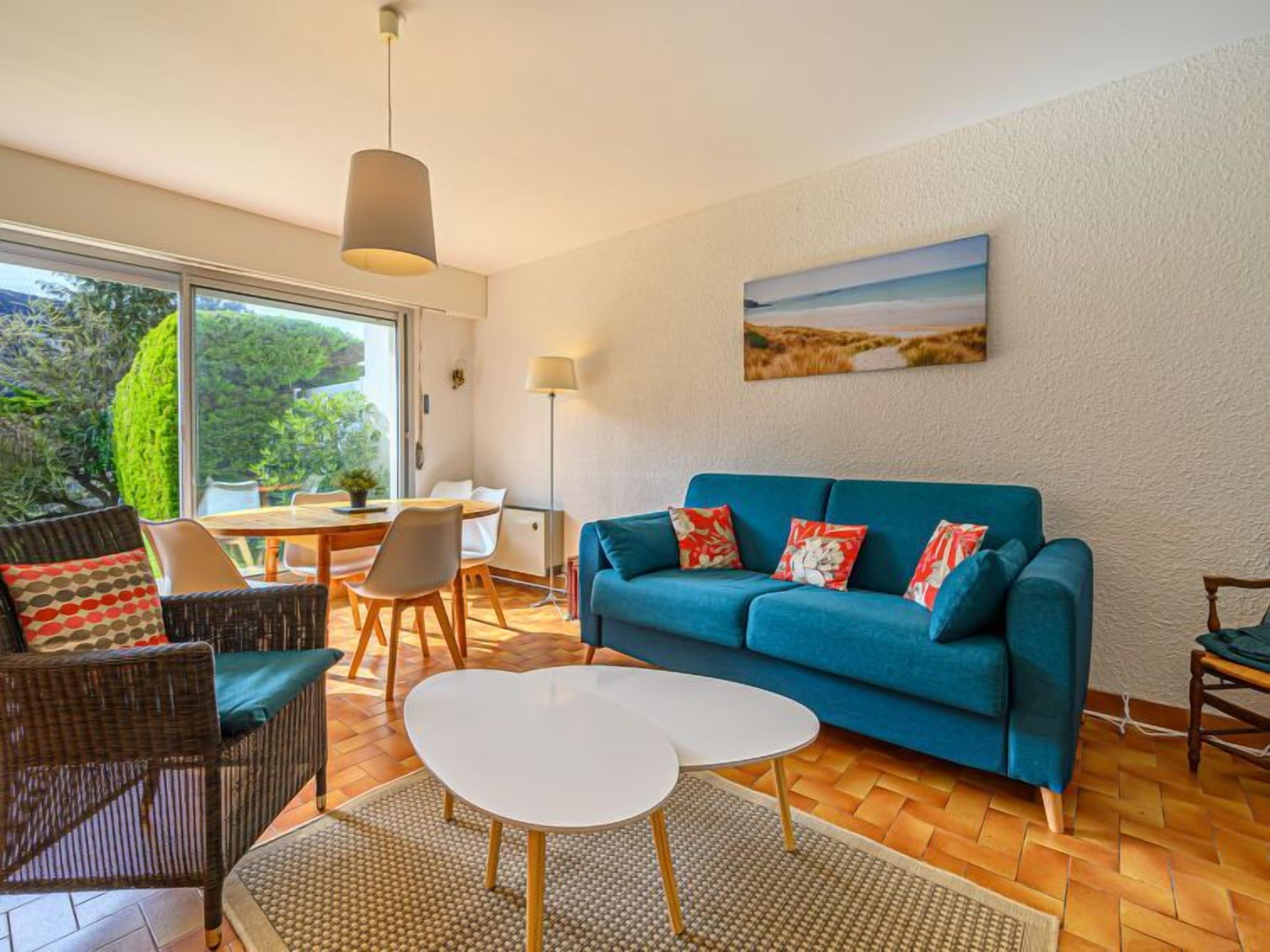 A modern living room with a blue sofa, wicker chairs, a white coffee table, and a dining area with a table and chairs.