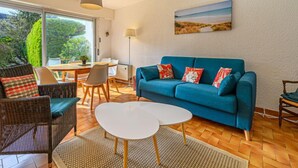 A modern living room with a blue sofa, wicker chairs, a white coffee table, and a dining area with a table and chairs. - La Sauvagère by Interhome (Carnac)
