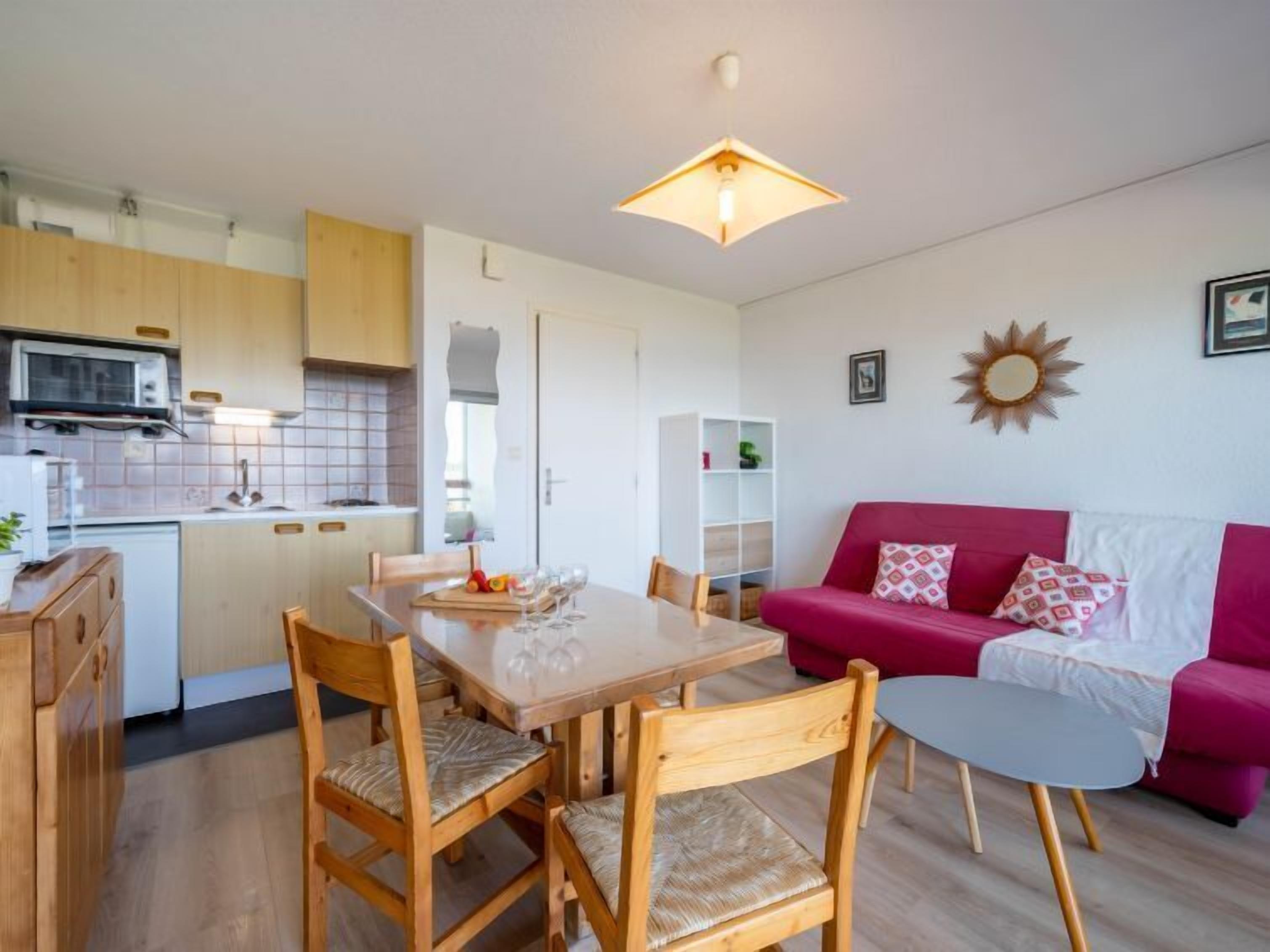 Un espace de vie compact comprenant un coin repas, une kitchenette et un canapé rouge.