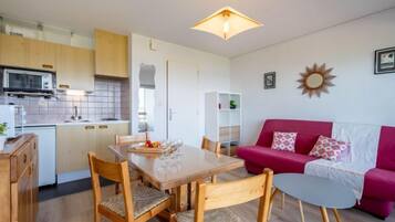 Un espace de vie compact comprenant un coin repas, une kitchenette et un canapé rouge.