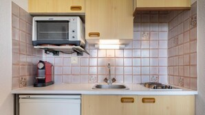 A compact kitchenette with a built-in oven, a coffee maker, and a sink. - Apartment MEN DU by Interhome (Carnac)