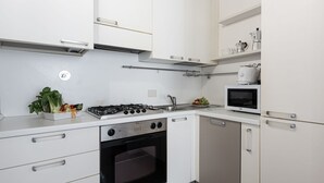 A modern kitchen with white cabinets, a gas stove, an oven, a microwave, and a sink.