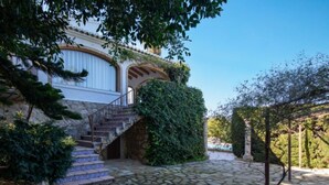 A stone-paved courtyard with a staircase leading to a white building with arches and a covered area with greenery. - Villa Bellavista by Interhome (Jávea)