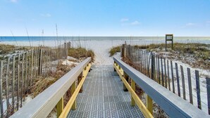 Une promenade en bois menant à une plage, dont le sol est constitué d’une grille métallique.