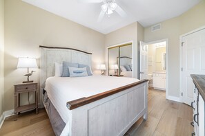 Ein Schlafzimmer mit Bett, Nachttischen, Deckenventilator und einem durchgegangenen Tür erkennbaren Badezimmer.