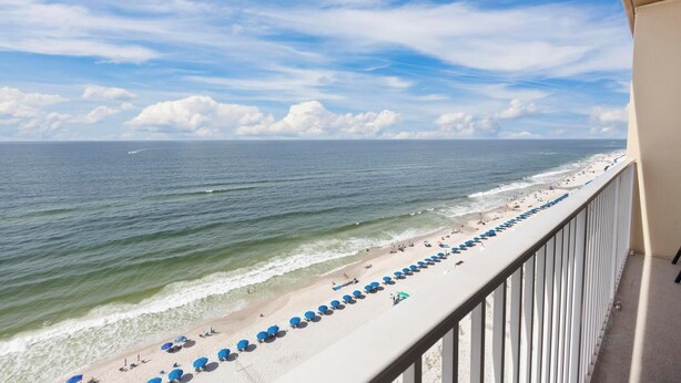 A balcony with a view of a beach with umbrellas and people.