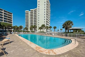 A swimming pool with lounge chairs, a gazebo, palm trees, and high-rise buildings in the background.