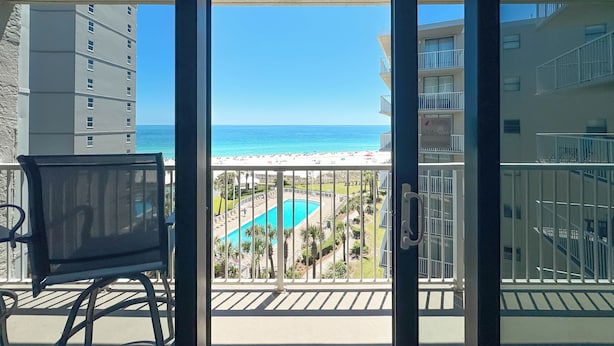Un balcón con vista a una piscina, edificios cercanos y una playa.