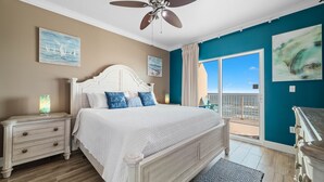 Une chambre avec un lit blanc, un ventilateur de plafond, une table de chevet avec une lampe et une vue sur l’extérieur grâce à une porte coulissante.