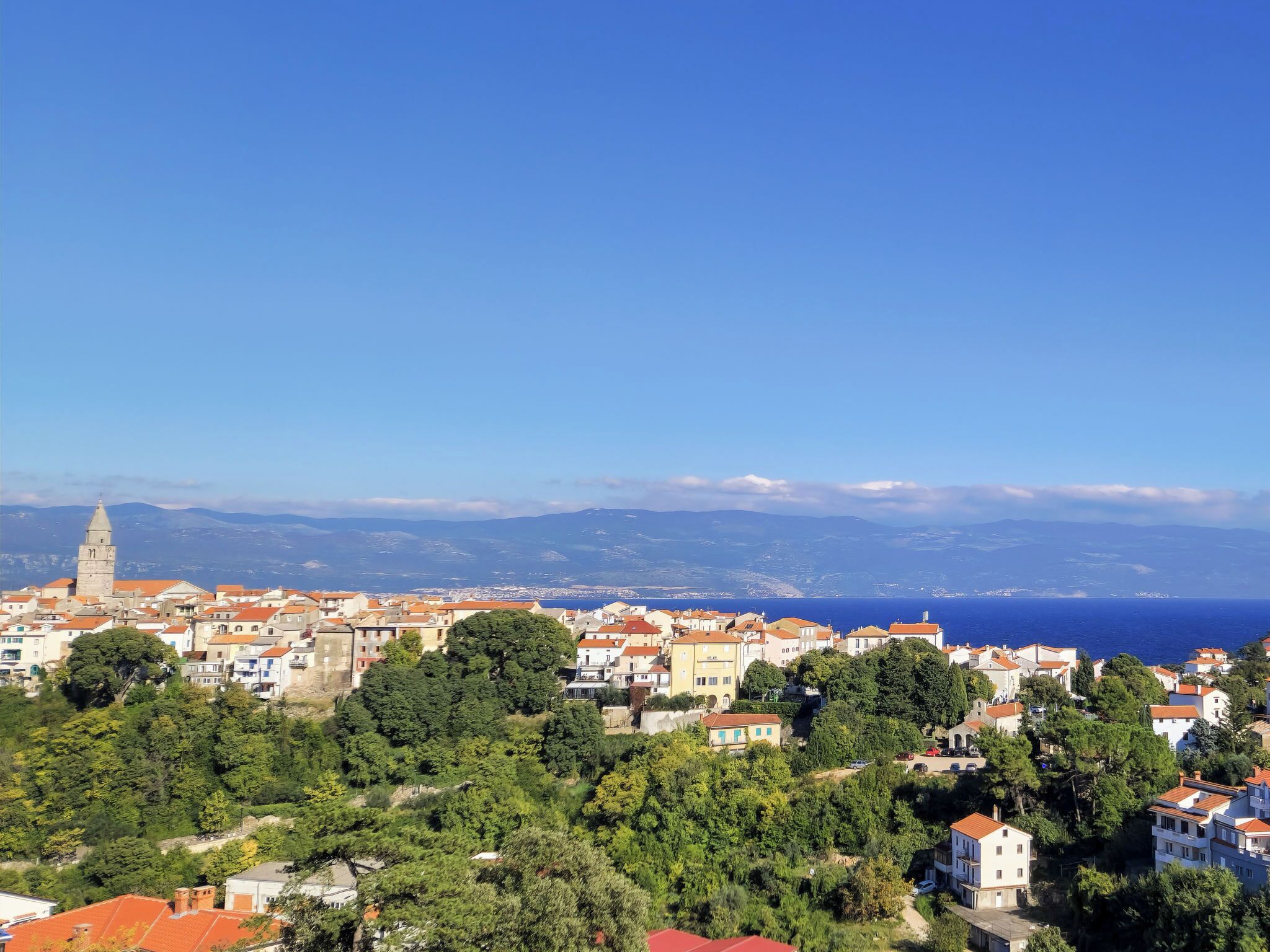 A coastal town with a prominent tower, dense greenery, and a clear view of the sea.