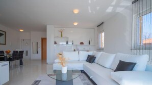 Un salon moderne avec une table basse en verre, un canapé blanc et un coin repas comprenant une table et des chaises.