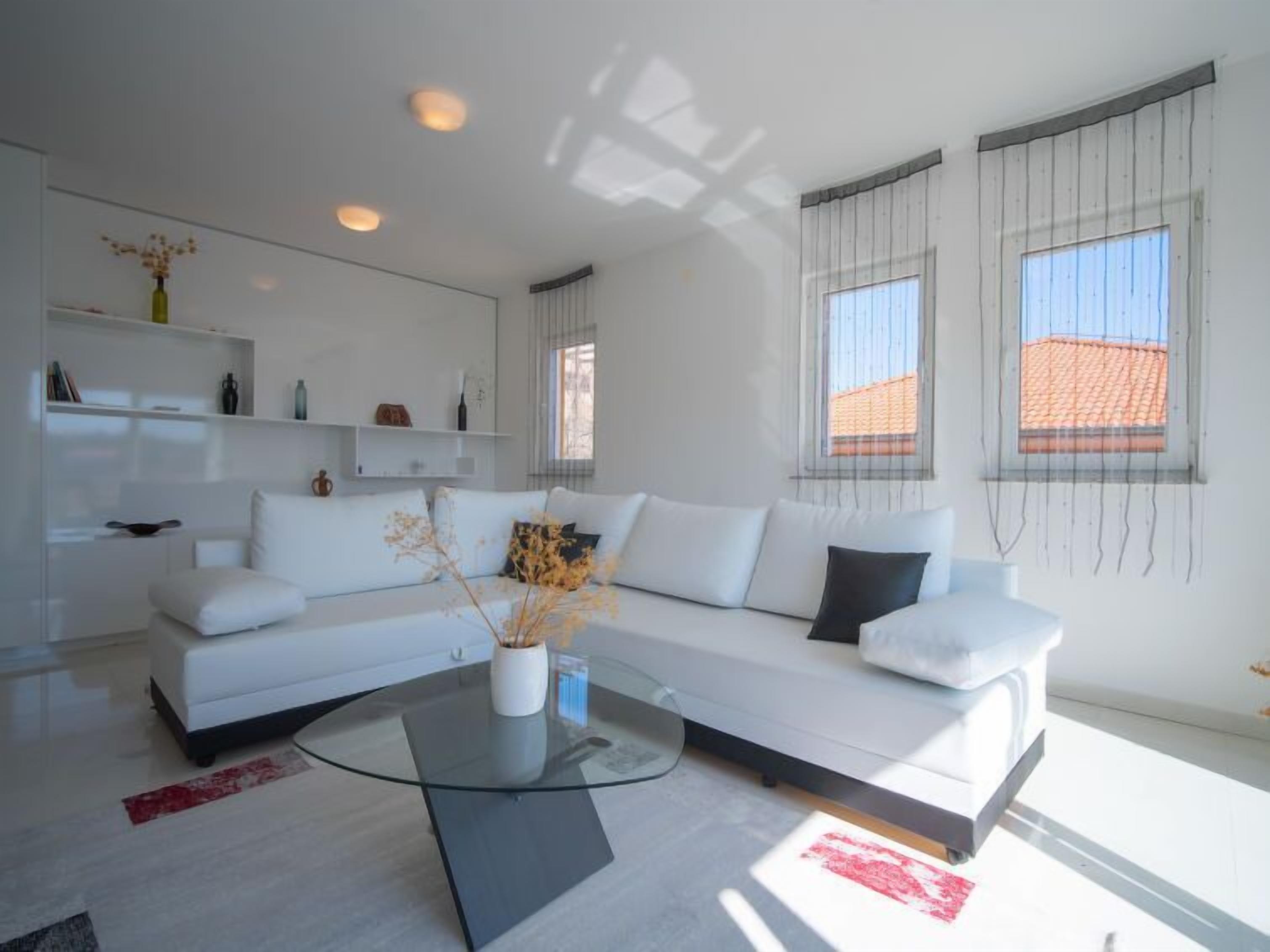 Ein modernes Wohnzimmer mit einem weißen Sofa, einem Glastisch und schlichter Einrichtung.