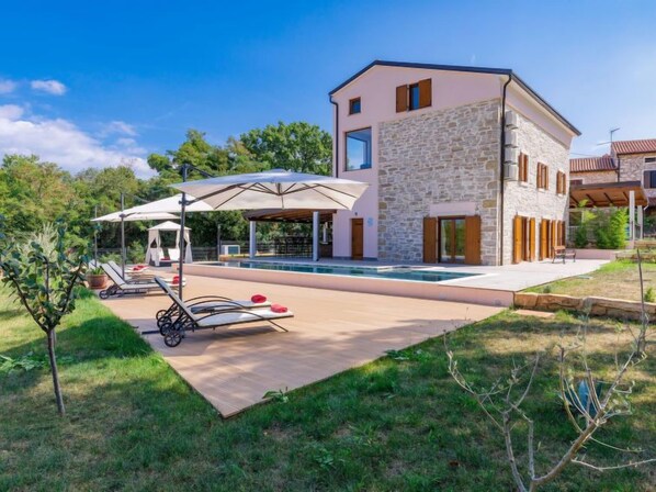 Una casa moderna con piscina, mobiliario exterior y fachada de piedra.