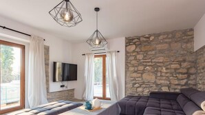 Una sala de estar moderna con una pared de piedra, un sofá grande, un sofá más pequeño y una mesa con un televisor montado en la pared.
