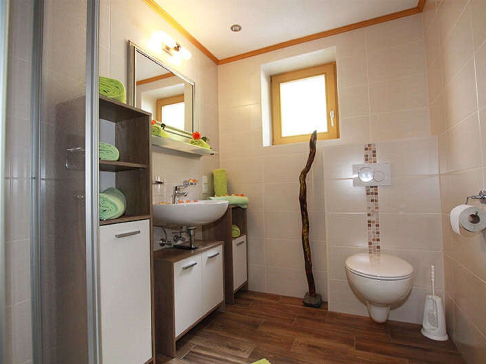 Une salle de bain avec un plancher en bois, un lavabo blanc, un miroir, des toilettes et un espace douche.