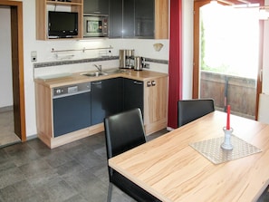 A compact kitchen with a microwave, stove, and sink. There is a dining table with chairs and a candle on the table.