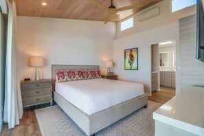 A bedroom with a large bed, bedside tables, a ceiling fan, and a painting on the wall.