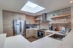 A modern kitchen with a skylight, built-in appliances, and a stone backsplash. - Oceanfront Luxury Condo w/ Hot Tub & Pool (Solana Beach)