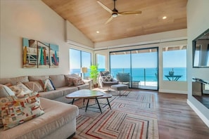A spacious living room with a large sofa, a coffee table, and a view of the ocean through large windows. - Oceanfront Luxury Condo w/ Hot Tub & Pool (Solana Beach)