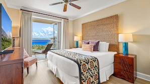 A hotel room with a bed, a desk, a chair, a nightstand, a lamp, and a view of the ocean.