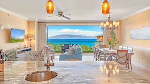 A spacious living area with a large kitchen island, a dining table, and a view of the ocean.